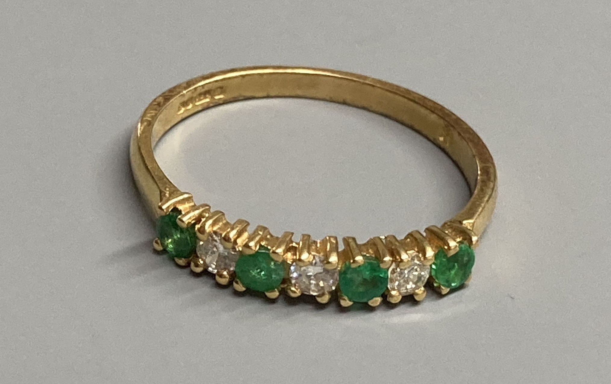 A modern 18ct gold, four stone emerald and three stone diamond set half hoop ring, size M/N, gross 2.1 grams.